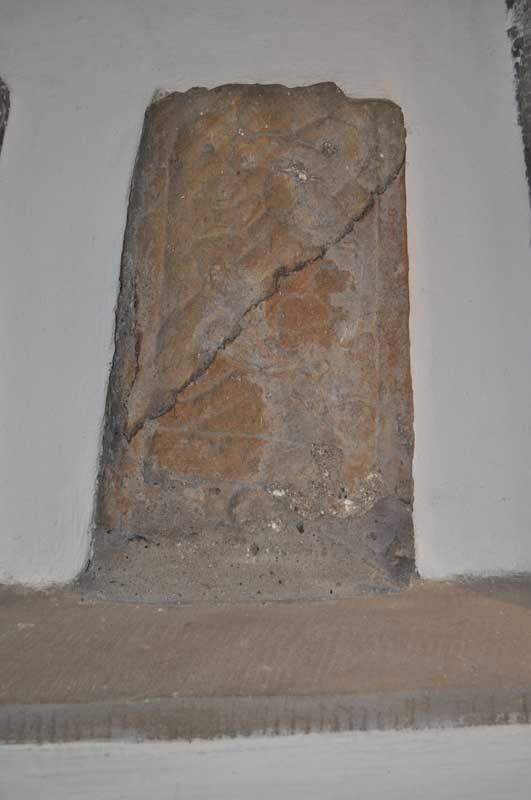 The lower half of a cross-shaft dating from the late 10th, early part of the 11th century showing a complete ring knot.  Displayed in a niche on the north wall of the nave.  