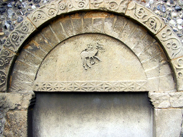 Carved animal above the tympanum. A stag, a horse or the Agnus Dei?  Why has the head of the animal been defaced?
Saxo-Norman south and west doorways.

Essex. TL 507228