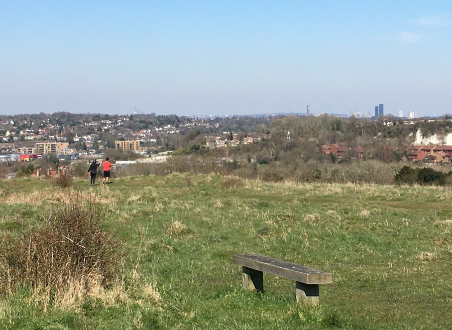 A couple look over towards Canary Wharf and the view of London. The map shows four Anglo-Saxon barrows here. The most visible barrow is just to their right.