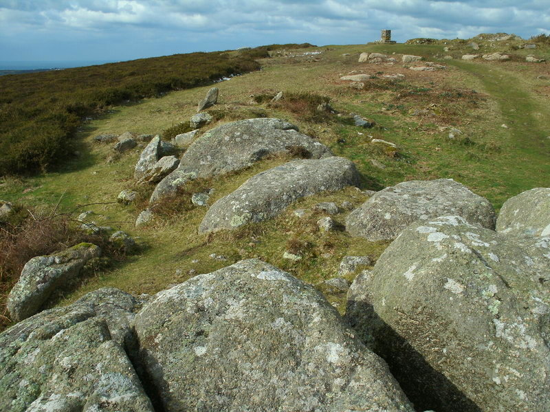 Carn Brea Neolithic long cairn. Centred at SW 38572798 is an elongated mound with kerb attached to an outcrop. It is oriented N-NW to S-SE. It is 26m long and from 5m to 6m wide, in a crest situation above a slight south slope, whereby it is clearly visible from the south east and all around to the west or seaward side.