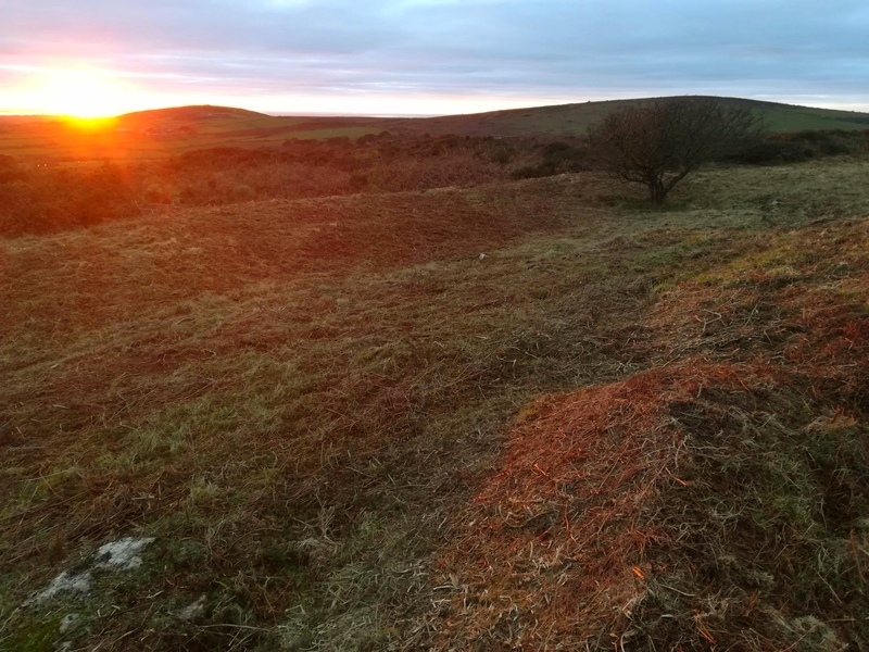 Bran Hillfort, The setting Winter sunlight shines upon the unfinished Western side of the Fort, Bartine hill with its prehistoric enclosure is in the background on the right and the setting sun is to the left of Carn Brea with all its ancient cairns at the left of the photo