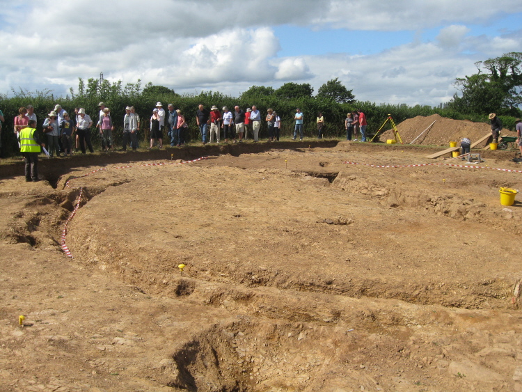 Looking across the site to NW with the tree-throw hole in foreground and the S to W arc of the large ring ditch.  Another group is gathered along the narrow western viewing edge of the dig.