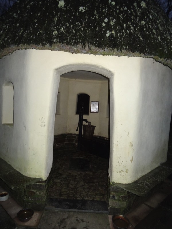 Looking into the little round building, showing the pump and the glass panel over the water of the holy well, centre.  I see that someone has kindly catered for dogs, with several bowls outside!