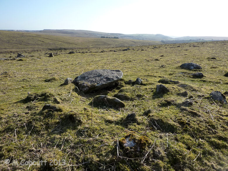 Legis Tor Cairn 2 has its cist still well defined by two side stones; its capstone offset to the south, and much of its encircling kerb still present. 

View here south