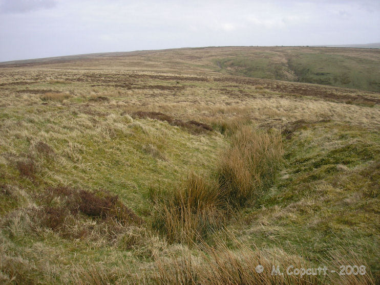 This large round barrow on the southeastern slopes of Chapman Down has a large slice cut through to the middle, rather than the usual hole in the top. 
View here to the southeast, with the steep valley down towards Challacombe seen, where the Longstone stands at the top of. It can be seen on a better res version of the picture, about 2/3 from the left below the skyline. 