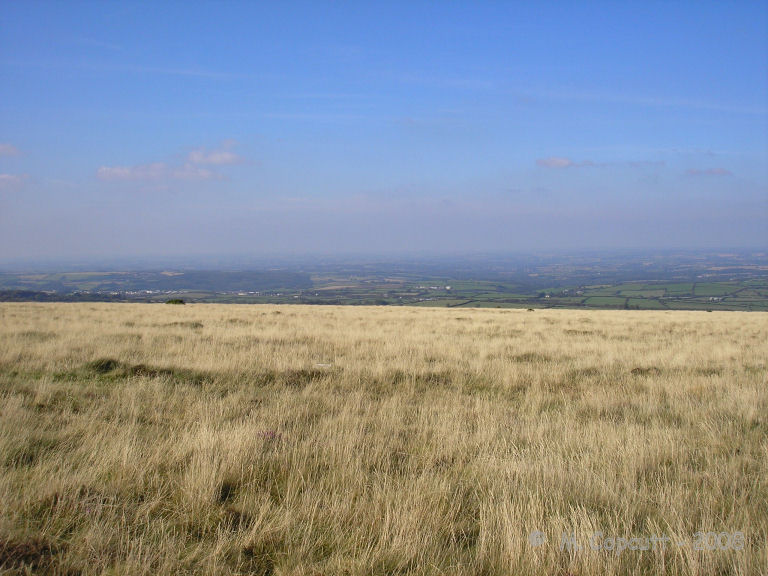 View looking northwest over the possible site of Sticklepath stone circle, clearly showing the flat shelf of land on the slopes of Cosdon Hill, and views for miles into the distance. 
A couple of stones can be seen if you look carefully.
