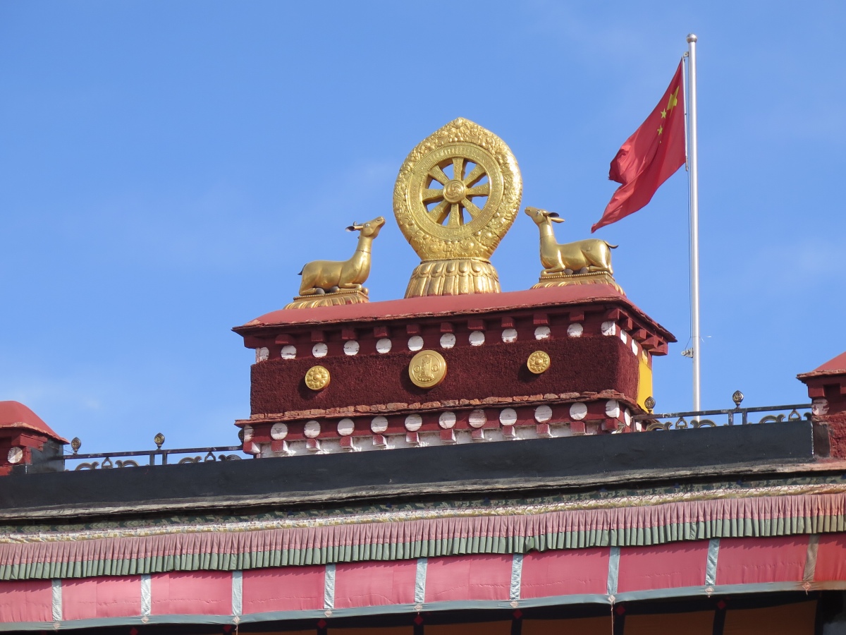 The twin deer and Dharma wheel emblem above the entrance to the Jokhang, with the ubiquitous Chinese flag next to it.  December 2019