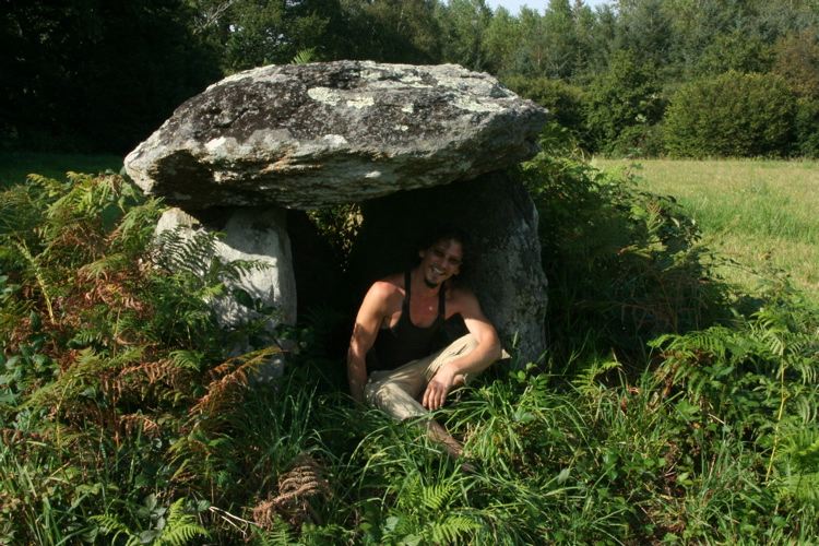 A tiny dolmen sitting in the middle of a field by the roadside. 
