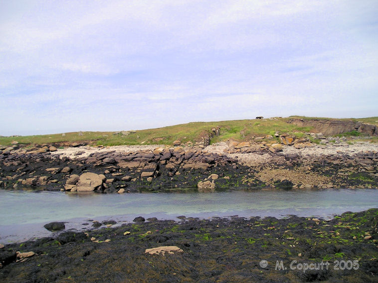 View of Ile Melon from the end of the little harbour wall on the mainland. 
The remains of two menhirs can be seen to the left of the picture, while the remaining dolmen is at the top of the island. 