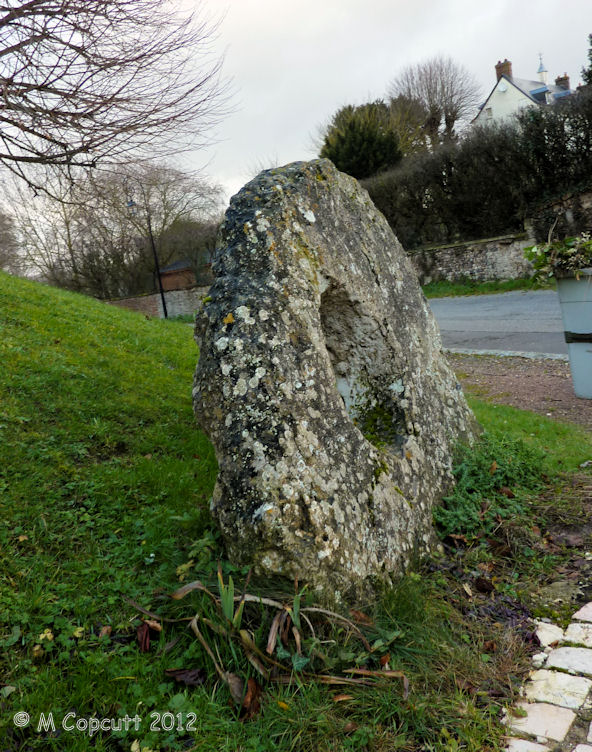 This wonderful holed stone is today found nicely presented just outside the little church of the village of Aizier, right on the banks of the River Seine. The stone is the portholed entry stone from a now destroyed allée couverte, destroyed during the making of a road. 

The stone is about 1.7 metres tall and wide, thickness 22 cm, but the important dimension is that of the circular hole, which