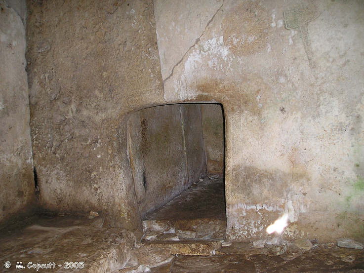 At the far corner of the main chamber, is found another entranceway into a further chamber. 

The entranceway is carved from two well fitted slabs, and has two grooves carved around it, rather like moulding round a more modern doorway. 

Above and to the right of this doorway, in the main chamber is a very visible axe carved onto the wall slabs.