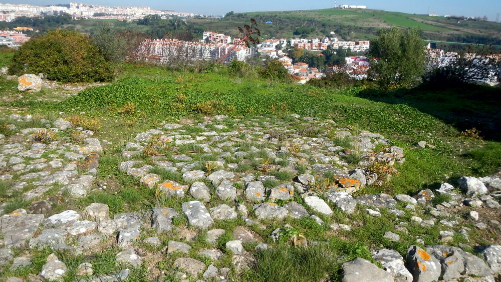 In the past this side was protected by a leaning rocky spur over the valley of the river of Barcarena. Nowadays nothing remains since the stone of the cliff was used as a quarry. In the front is still possible to see the pavement of the round structures.
