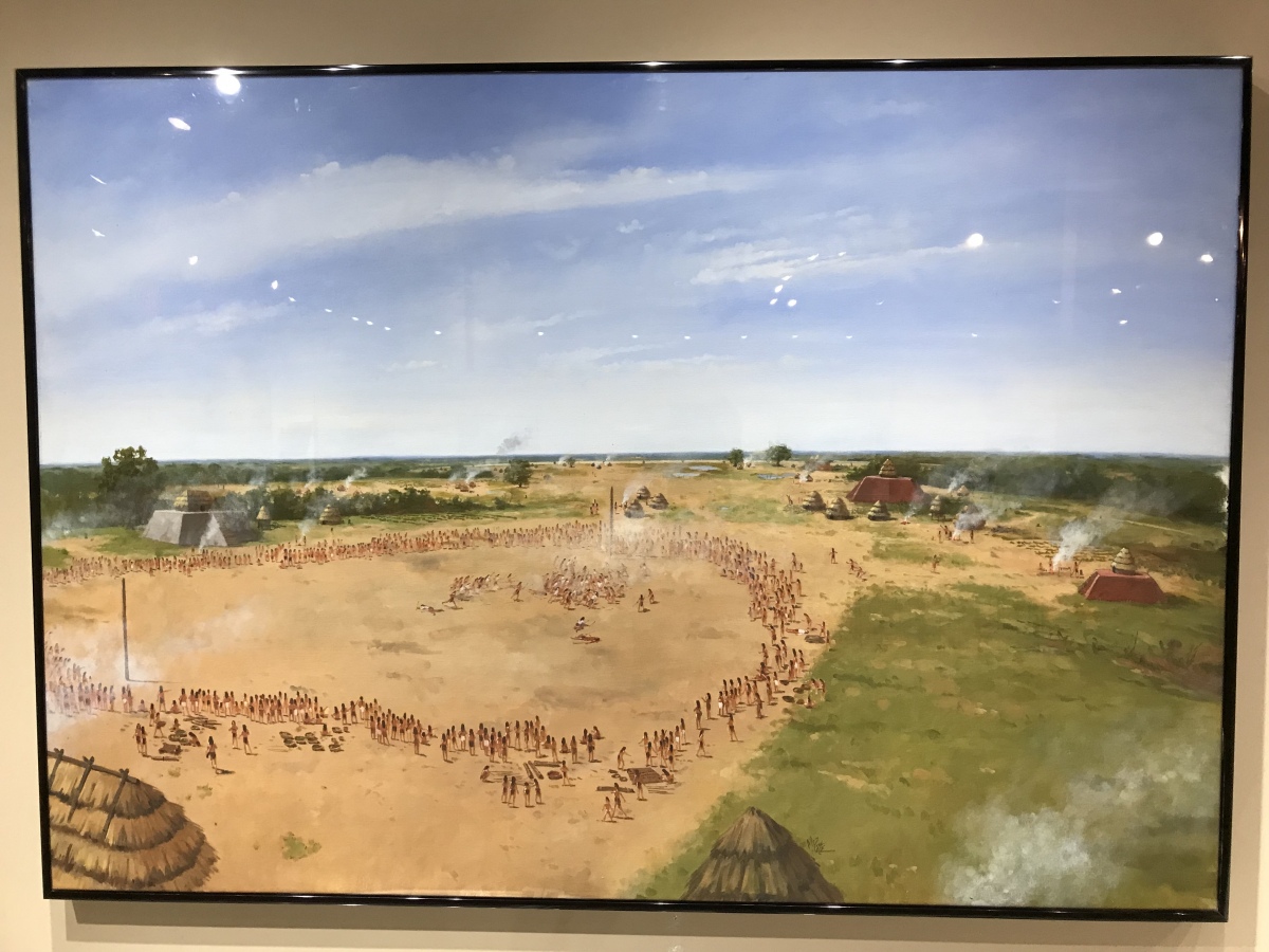
National Park Service illustration of the Shiloh, Tennessee mound complex. (Yes, it is located in the Civil War battlefield park.) The illustration shows several of the platform mounds, several of which were covered in a bright red clay. People are gathered in the central plaza area and a game is taking place. There are 8 mounds and a couple dozen smaller house mounds there and the site was encl