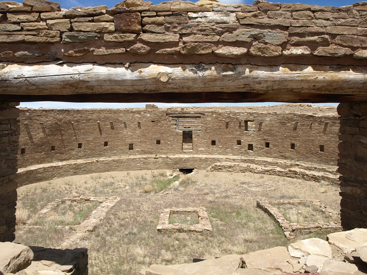View through the south doorway, showing two of the circular base structures for roof posts, the center square firebox, and the two rectangular floor structures.
Photo by bat400, April 2012.