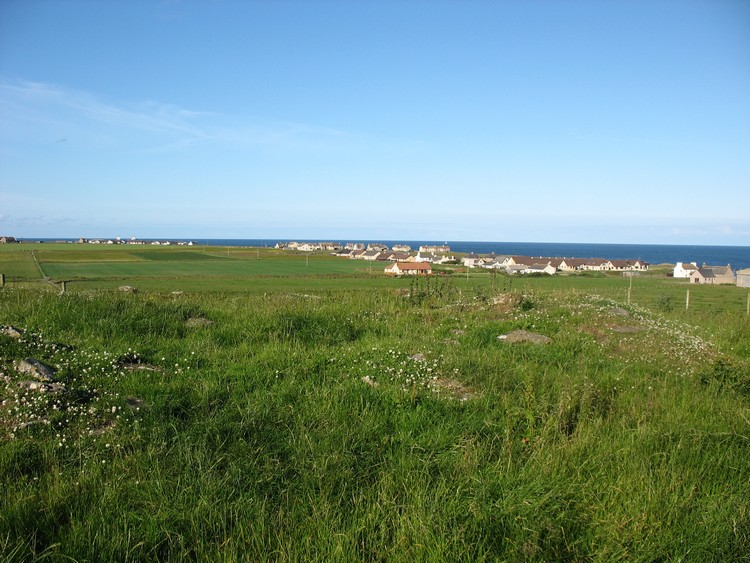 The Pap broch with distinguishable circular shape of the wall and view towards village of Papigoe (photo taken on July 2011).
