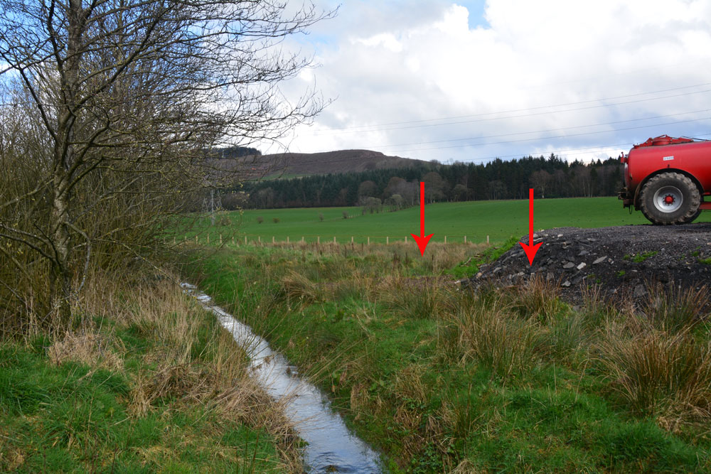 The two arrows show approximately where the two cairns should be - one buried (almost buried?) by the new hardstanding area; the other further back in the field. Photograph taken from the corner of the field at NY 11832 96456.