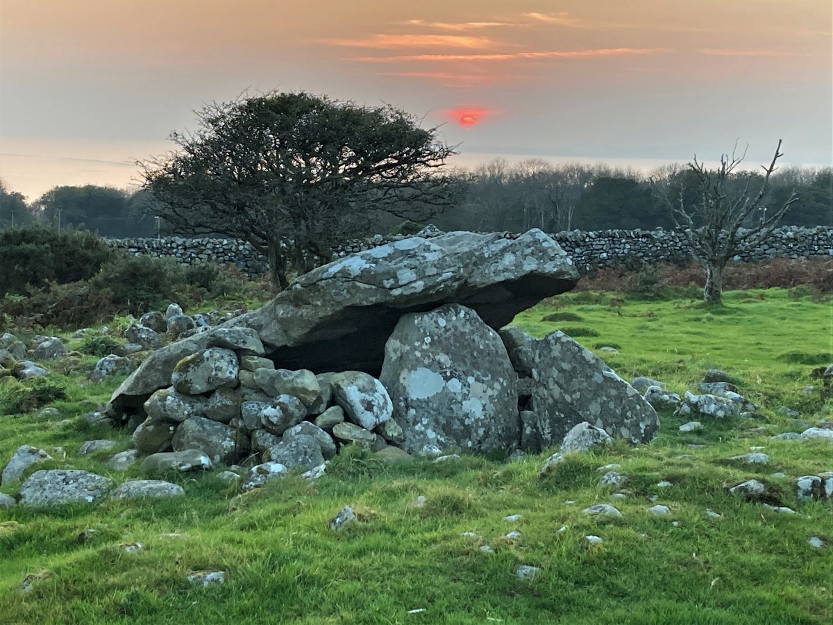 The autumn equinox sun slips into cloud over the sea, as it sets behind Cors y Gedol chambered tomb.