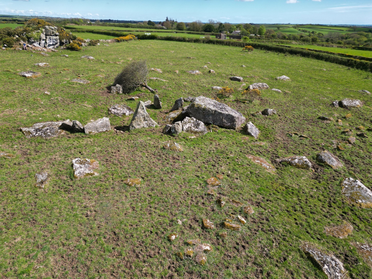 showing the collapsed capstone, measuring 5.0m by 3.5m by 1.0m, that has prostrated three orthostats; remains of this chambered tomb in an area of outcropping rock and erratic boulders, whilst six stones, the largest 2.5m high, define a forecourt to the north-east.