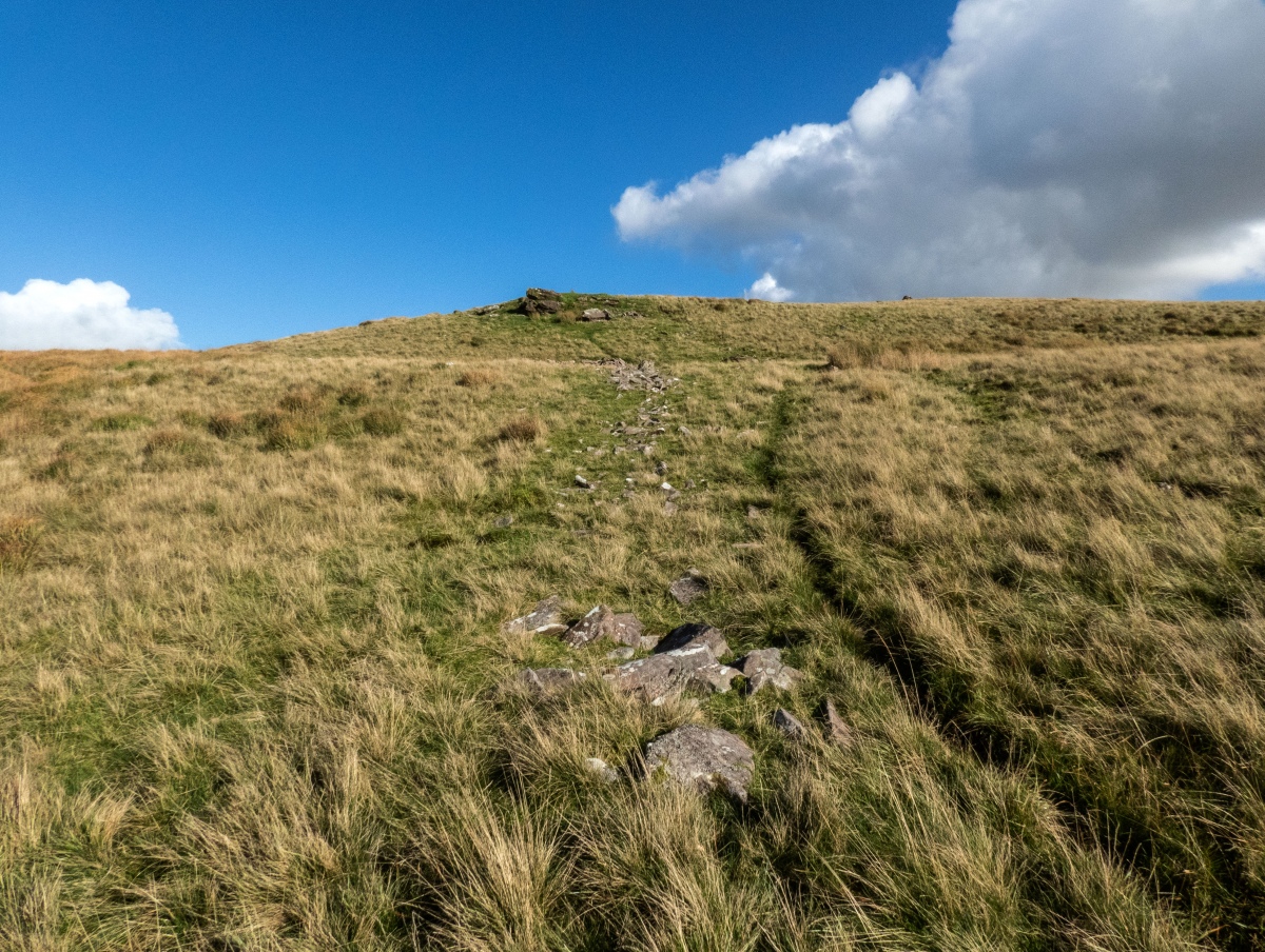 The ruined wall, looking back towards the Western cairn, which lies just below the outcrop.
  The summit cairn can be seen to the right here.